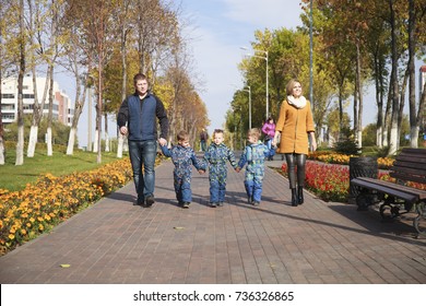 Young Parents Walking With Triplets In The Autumn Park