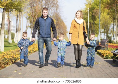 Young Parents Walking With Triplets In The Autumn Park