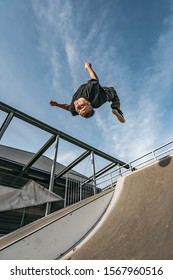 Young Parkour And Freerunning Athlet Doing A Backflip From A Wall In An Urban Enviroment With A Blue Sky In De Background, Jumping Tumbling  Gymnastics Training Concept