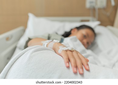 Young Patient Asian Woman Lying On Bed In Hospital With IV Saline Drip To Back Of The Hand, Teenager Sick In Hospital, Selective Focus, Healthcare And Health Insurance Concept.