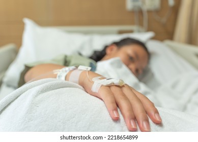 Young Patient Asian Woman Lying On Bed In Hospital With IV Saline Drip To Back Of The Hand, Teenager Sick In Hospital, Selective Focus, Healthcare And Health Insurance Concept.