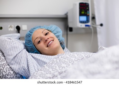 Young Patient In Scrub Cap Recovering After Surgery In Post Operative Care Room In Modern Hospital. Woman With Pulse Oximeter After Operation Monitored By Doctor In Recovery Room Of Orthopedic Clinic.