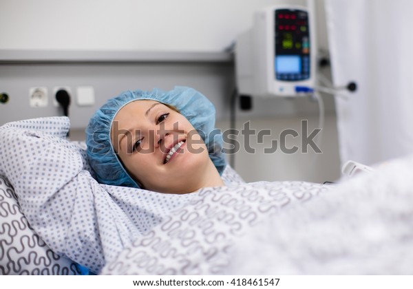 Young patient in scrub cap recovering after\
surgery in post operative care room in modern hospital. Woman with\
pulse oximeter after operation monitored by doctor in recovery room\
of orthopedic clinic.