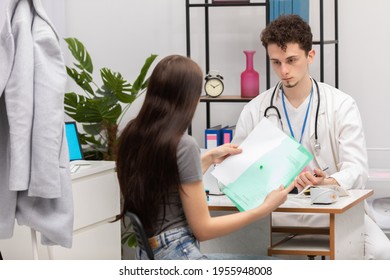 A Young Patient Takes Lab Results Out Of Her Folder. Primary Care Physician. Doctor's Office