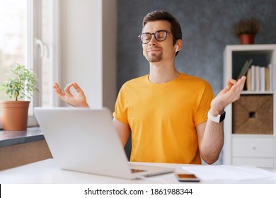 Young peaceful mindful man keep calm, smiling, relaxing, meditating while working remotely from home with laptop, doing yoga breathing exercises. Online education, social distancing. Stay home, covid
