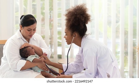 Young Pediatrian Checking The Well Being Of Little Baby Boy Who's Crying In Mother's Arms. Health And Well Being Concept.