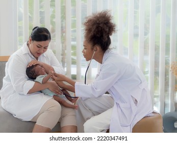 Young Pediatrian Checking The Well Being Of Little Baby Boy Who's Crying In Mother's Arms. Health And Well Being Concept.