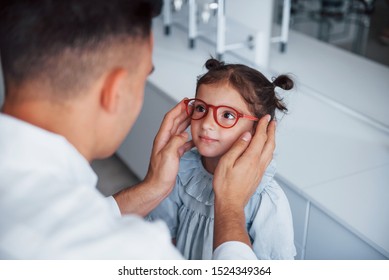 Young Pediatrician In White Coat Helps To Get New Glasses For Little Girl.