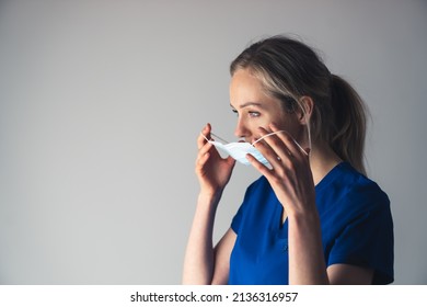 Young Pensive Caucasian Female Surgeon Putting On Or Taking Off Her Face Mask. High Quality Photo