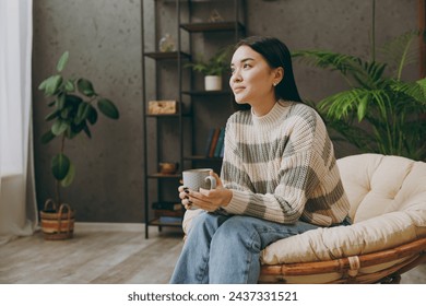 Young pensive happy woman wears casual clothes sits on armchair hold cup drink coffee look camera stay at home hotel flat rest relax spend free spare time in grey living room indoor. Lounge concept - Powered by Shutterstock