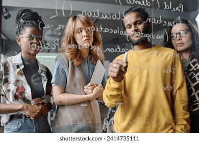 Young pensive programmers working in team on code written on glass wall in office