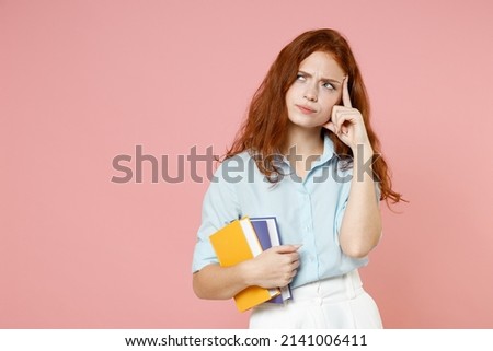 Young pensive puzzled redhead student woman wear blue shirt hold book looking aside prop up forehead isolated on pastel pink background studio portrait Education high school university college concept