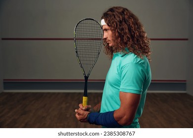 Young pensive racketball player with racket standing backside