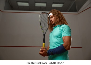 Young pensive racketball player with racket standing backside