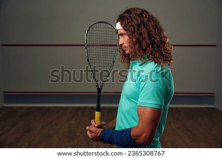 Young pensive racketball player with racket standing backside