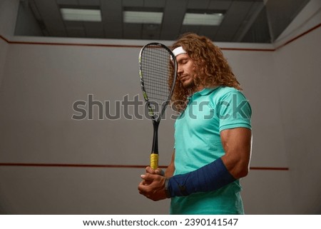 Young pensive racketball player with racket standing backside