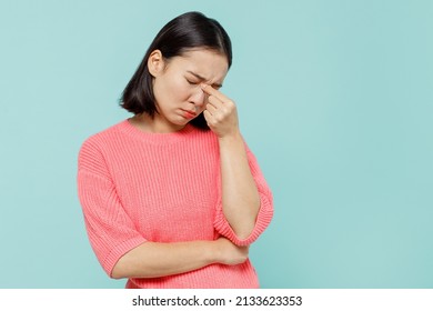 Young pensive sad woman of Asian ethnicity 20s wearing pink sweater keep eyes closed rub put hand on nose isolated on pastel plain light blue color background studio portrait. People lifestyle concept