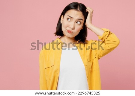 Young pensive thoughtful mistaken sad woman of Asian ethnicity wears yellow shirt white t-shirt scratch hold head look aside isolated on plain pastel light pink background studio. Lifestyle concept
