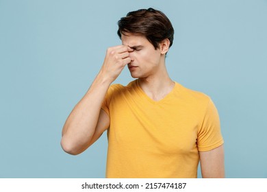 Young Pensive Tired Sad Exhausted Thoughtful Minded Man 20s Wear Yellow T-shirt Keep Eyes Closed Rub Put Hand On Nose Isolated On Plain Pastel Light Blue Background Studio. People Lifestyle Concept