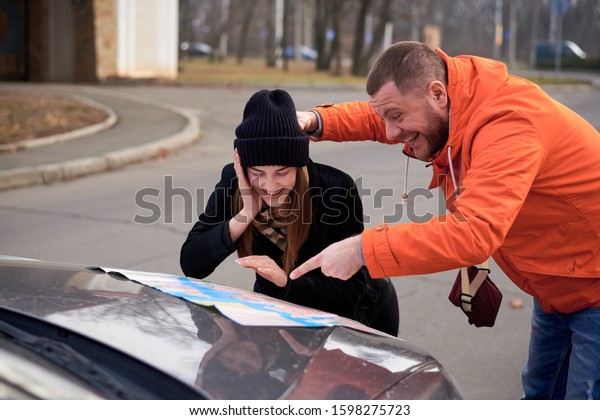 Young\
people argue near a car with a map on the\
road.