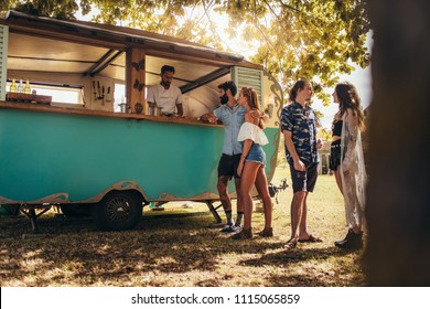 Young people buying street food from a food truck at park. Group of men and woman at food truck. - Powered by Shutterstock