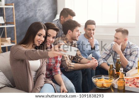 Young people in casual clothes are resting with pizza and bottles of drink. Girls making selfie while boys talking. Friendship, leasure, rest, home party concept