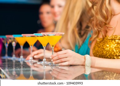 Young people in club or bar drinking cocktails and having fun; close-up on glasses on the bar