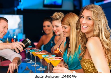 Young People In Club Or Bar Drinking Cocktails And Having Fun; The Barkeeper Is Mixing Drinks