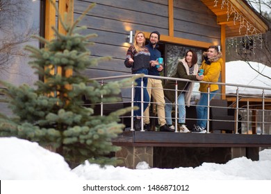Young people communicate on the veranda of the cottage and admire the winter landscape. Friends came to celebrate the New year in a country house. Talking and drinking tea on the balcony of the house