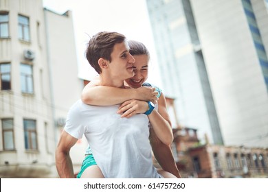 Young People, Couple Having Date On The Street. A Loving Couple On A Date On A Summer Evening. The Guy With The Girl Hugs And Kisses. Youth, First Feelings, First Love, First Dates. The Girl Jumps The