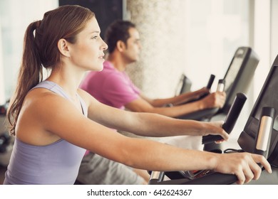 Young People Cycling Exercise Bike In Fitness Club