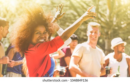 Young people dancing in forest party on summer time - Happy friends drinking cocktails and laughing together outdoor in music festival - Focus on black girl face - Youth lifestyle and event concept - Powered by Shutterstock