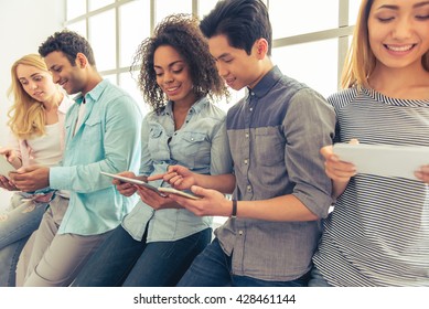 Young people of different nationalities are using gadgets, talking and smiling - Powered by Shutterstock