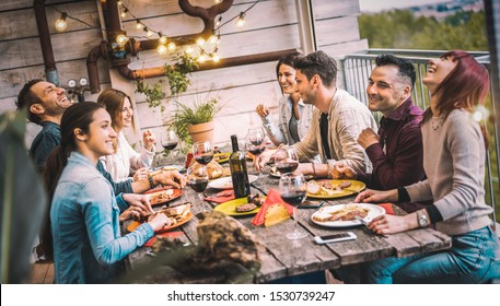 Young people dining and having fun drinking red wine together on balcony rooftop dinner party - Happy friends eating bbq food at restaurant patio - Youth life style concept on warm evening filter