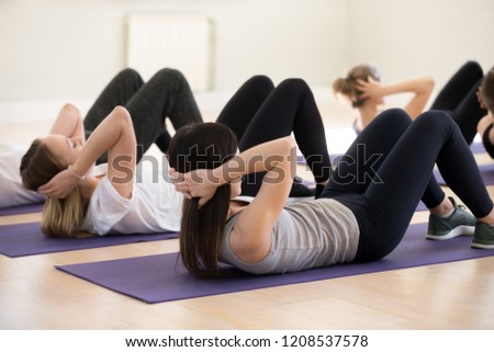 Image of abs crunches. Young people doing abs crunches lying on rubber carpet mats at gym. Millennial girls guys wearing sportswear and sneakers do stomach situp exercises indoors, side view. Wellbeing and wellness concept