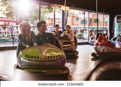 Young people driving bumper car at fairground. Young friends having fun riding bumper car at amusement park.