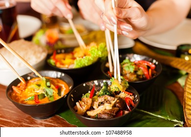 Young people eating in a Thai restaurant, they eating with chopsticks, close-up on hands and food