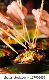 Young People Eating In A Thai Restaurant, They Eating With Chopsticks, Close-up On Hands And Food