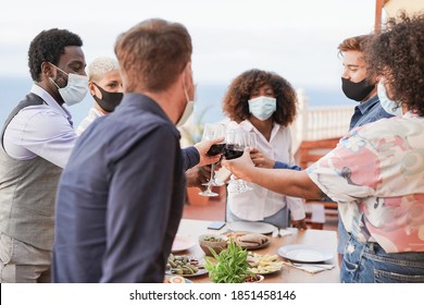 Young People Enjoy Dinner At Home On Patio And Cheering With Wine While Wearing Protective Face Mask For Coronavirus - Focus On The Hands