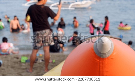 Young people enjoy swimming in the shallow waters of the sea during the hot summer obscured by the view of the inflatable banana boat tips. Blurs.