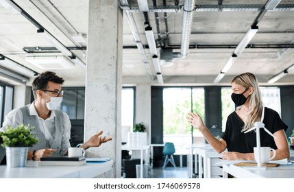 Young people with face masks back at work in office after lockdown. - Shutterstock ID 1746069578