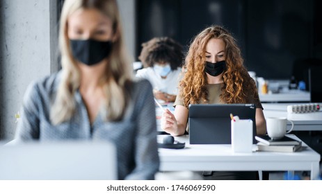 Young people with face masks back at work or school in office after lockdown. - Shutterstock ID 1746069590