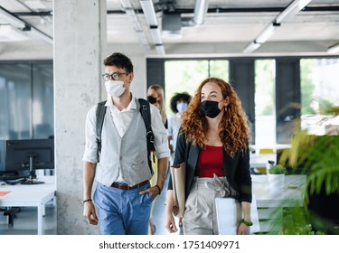 Young people with face masks back at work in office after lockdown, walking. - Powered by Shutterstock