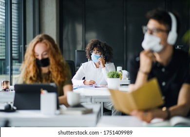 Young people with face masks back at work or school in office after lockdown. - Shutterstock ID 1751409989