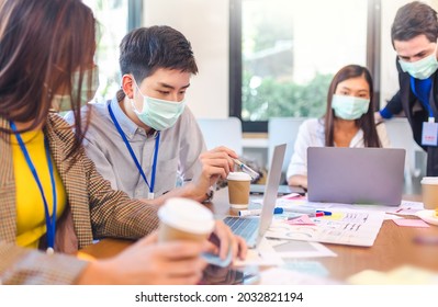 Young People With Face Masks Back At Work In Office After Lockdown.Asian Small Business Startup Multiracial Brainstorm Meeting With Laptop And Chart Paper Everyone Mask For Covid19 Protection Corona.