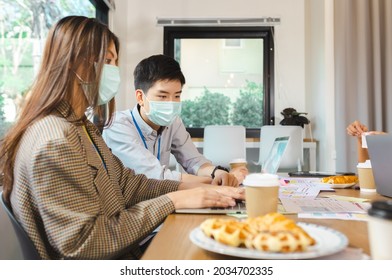 Young People With Face Masks Back At Work In Office After Lockdown.Asian Small Business Startup Multiracial Brainstorm Meeting With Laptop And Chart Paper Everyone Mask For Covid19 Protection Corona.