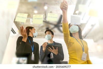 Young People With Face Masks Back At Work In Office After Lockdown.Asian Small Business Startup Multiracial Brainstorm Meeting With Laptop And Chart Paper Everyone Mask For Covid19 Protection Corona.