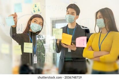 Young People With Face Masks Back At Work In Office After Lockdown.Asian Small Business Startup Multiracial Brainstorm Meeting With Laptop And Chart Paper Everyone Mask For Covid19 Protection Corona.