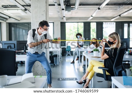 Young people with face masks back at work in office after lockdown, measuring distance.