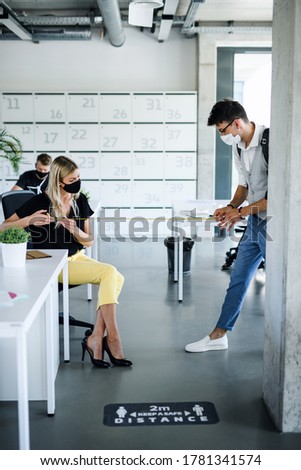 Young people with face masks back at work in office after lockdown, measuring distance.